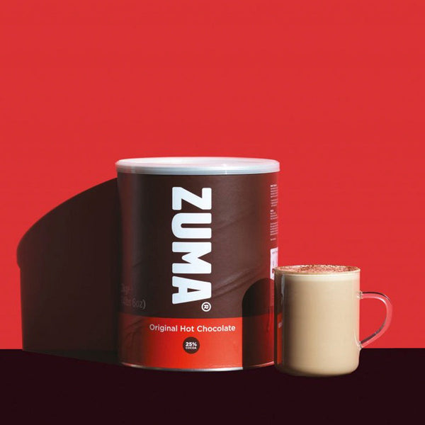 A red and brown metal 2kg tub of Zuma Original Hot Chocolate Powder. 25% Cocoa. Mug of hot chocolate to the right and a red backdrop