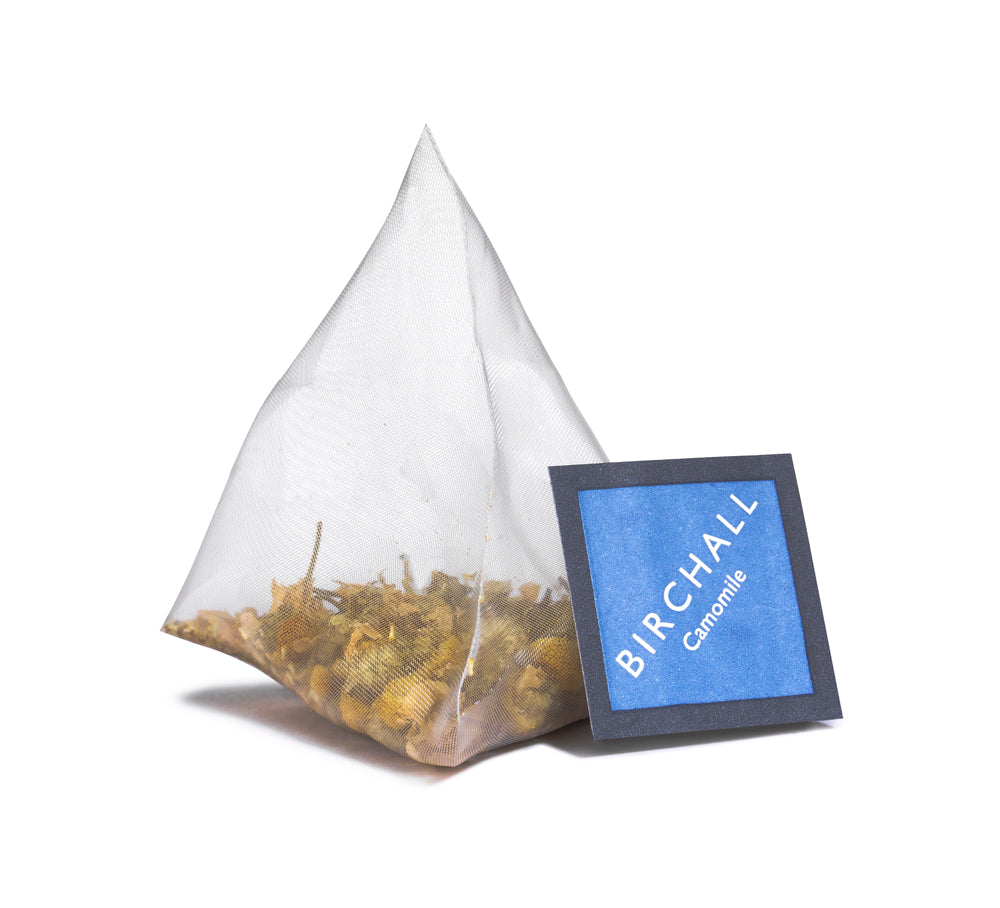 A single prism blue tagged tea bag of Birchall Camomile tea. Mesh tea bag with large loose leaf inside.