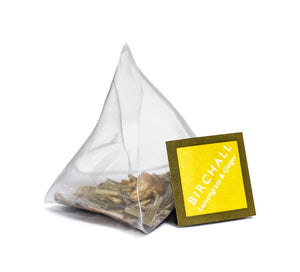 A single prism yellow tagged tea bag of Birchall Lemongrass & ginger tea. Mesh tea bag with large loose leaf inside.