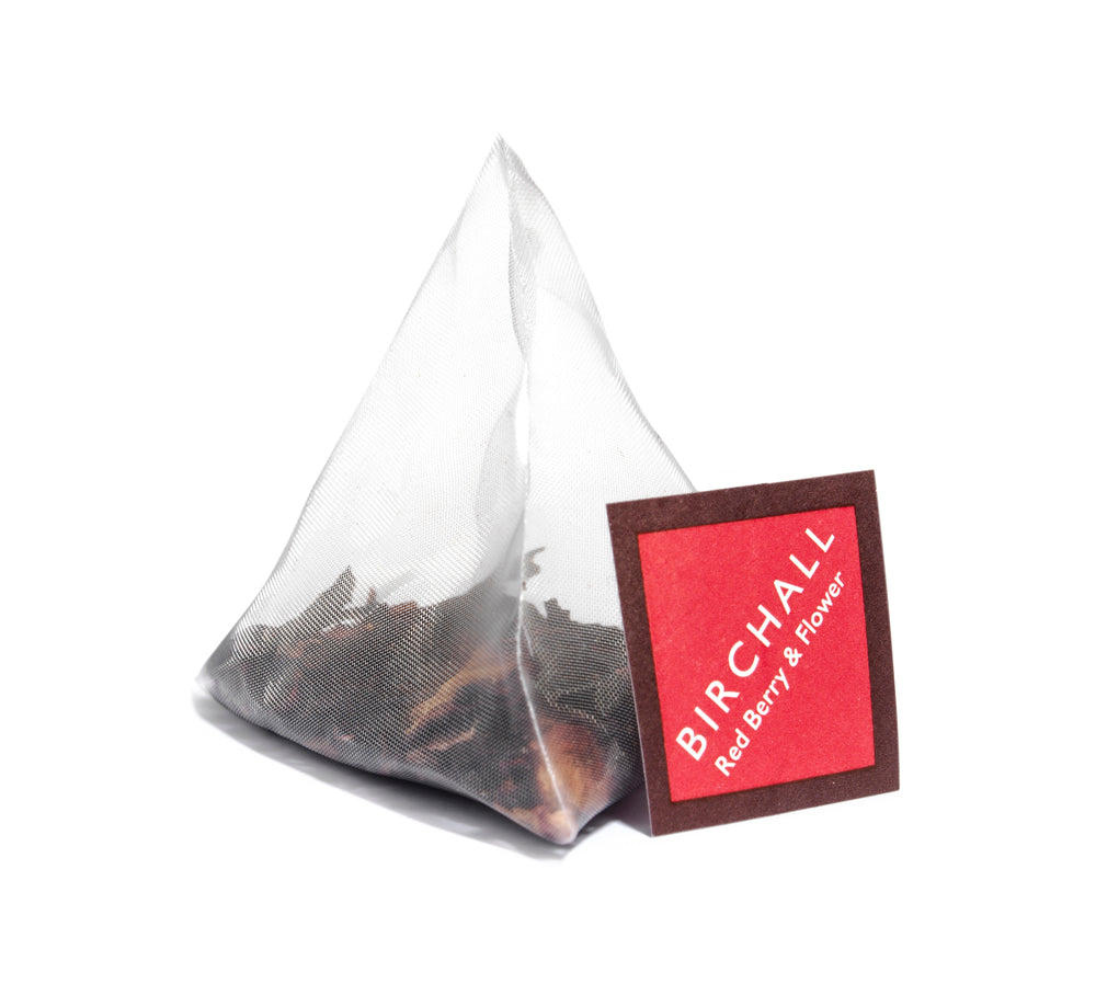 A single prism red tagged tea bag of Birchall Red Berry & Flower tea. Mesh tea bag with large loose leaf inside.