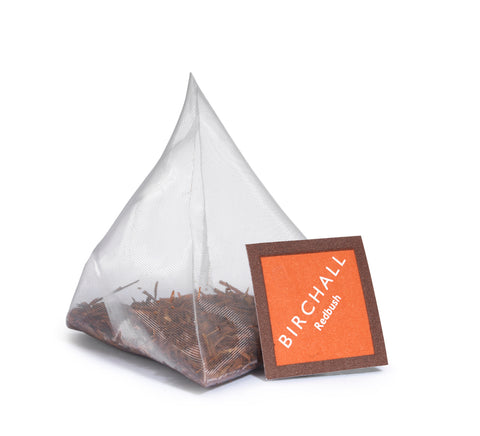 A single prism orange tagged tea bag of Birchall Organic Redbush tea. Mesh tea bag with large loose leaf inside.